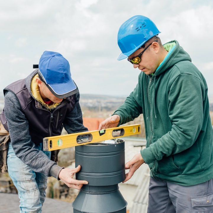 workers on the roof installing tin cap on the iron chimney